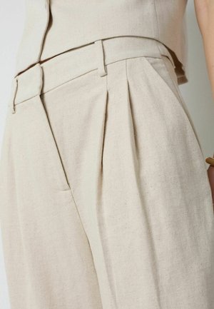 Kõrge vöökohaga beežid püksid esipragudega, vööaasade, küljetaskute ja tekstuurse kangaga, kantud sobiva lühikese topiga.