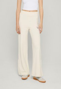 Kremowe spodnie szerokie na gumce, z dyskretnym czarnym logo z boku i gładką fakturą.