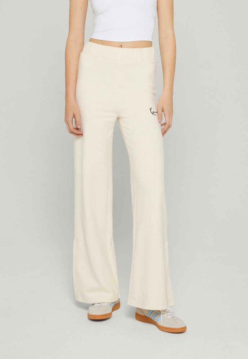 Kremowe spodnie szerokie na gumce, z dyskretnym czarnym logo z boku i gładką fakturą.