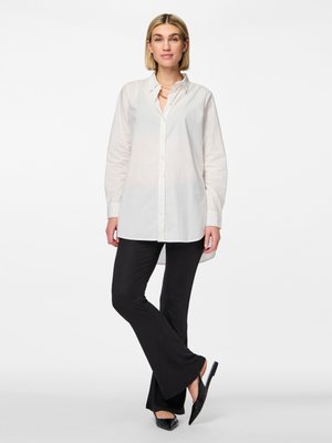 White, button-up shirt with long sleeves, paired with black, ribbed flared pants. Footwear features flat, black slip-on shoes.