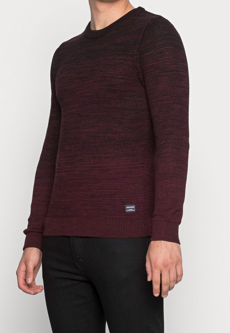 Burgunderfarbener Strickpullover mit strukturiertem Muster, Rundhalsausschnitt und gerippten Bündchen und Saum. Mit kleinem Markenlogo am unteren Ende.