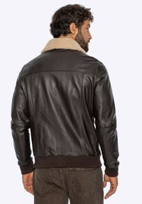 Bruine leren jas met een kraag van schapenvacht, geribbelde manchetten en zoom, en een aansluitend ontwerp. Het materiaal heeft een gladde textuur en minimale stikdetails.