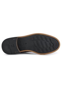 Suela de zapato de goma negra con una superficie texturizada y patrones verticales. Detalles en el borde en color marrón claro. Nombre de la marca y país de fabricación indicados.