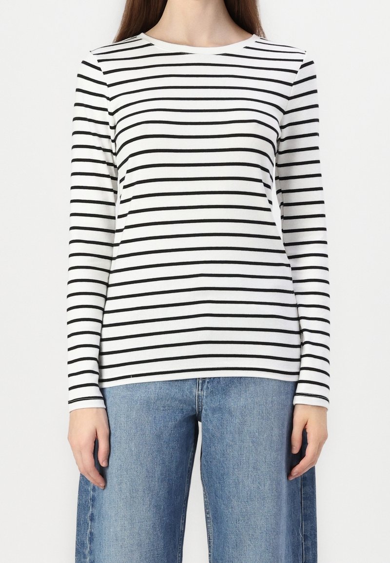 Dlouhý rukáv, triko s kulatým výstřihem v bílé barvě s černými vodorovnými pruhy. Měkká látka, přiléhavý střih a mírná pružnost. Kombinováno s světle modrými džínami.