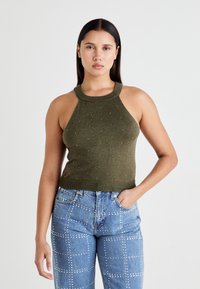 Top halter lavorato a maglia verde oliva con scollatura a costine e decorazioni sparse, abbinato a jeans azzurri chiari con motivi di borchie.