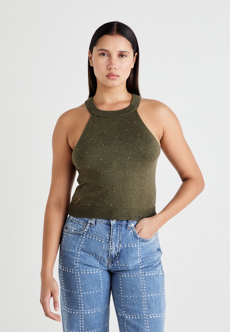 Top halter lavorato a maglia verde oliva con scollatura a costine e decorazioni sparse, abbinato a jeans azzurri chiari con motivi di borchie.