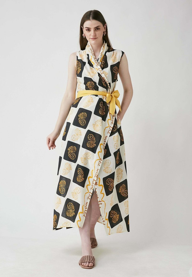 Maxi dress in white with black and gold floral pattern. Features a wrap design, sleeveless cut, and a tied yellow belt. Includes a side slit.