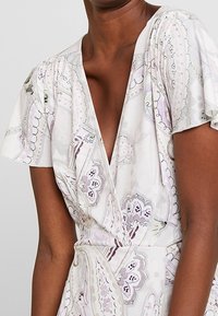 Floral-patterned dress in light colors, featuring short flutter sleeves, a deep V-neck, and a cinched waist for a fitted silhouette.