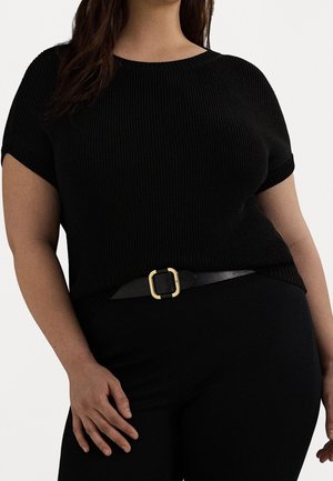 Mujer con una camiseta negra de manga corta acanalada, metida dentro de unos pantalones negros con un cinturón negro que tiene una hebilla cuadrada dorada.