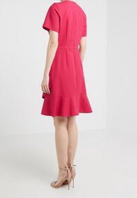 Fuksjowa sukienka do kolan z krótkimi rękawami, rozkloszowanym dołem i zamkiem błyskawicznym z tyłu. Noszona z cielistymi sandałami na wysokim obcasie. Gładka tekstura materiału.
