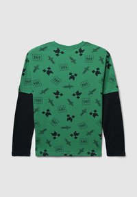 Maglietta a maniche lunghe verde con un motivo a tema Minecraft nero, con spade, blocchi di TNT e forme pixelate su una manica nera solida.