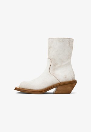 Bottine en cuir texturé blanc avec un bout pointu, un talon en bois empilé incliné et des coutures soignées sur un fond blanc.