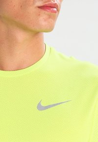 Camisa atlética de malla amarilla con mangas cortas, que presenta un logo de Nike gris en el área del pecho izquierdo y un escote redondo.