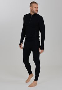 Schwarzes langärmliges Thermaloberteil mit einem Viertelreißverschluss und schmaler Passform, kombiniert mit passenden Leggings, die beide aus weichem, dehnbarem Material gefertigt sind.