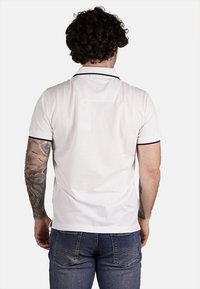 Polo bianca con maniche corte, bordo nero su colletto e estremità delle maniche, e finitura testurizzata; vista da dietro.