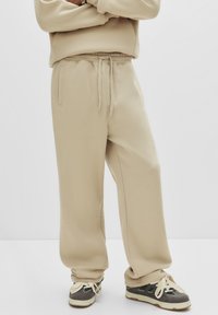 Beige sweats met een relaxte pasvorm, elastische tailleband en trekkoord. Zachte textuur met zijzakken, gecombineerd met donkere schoenen.