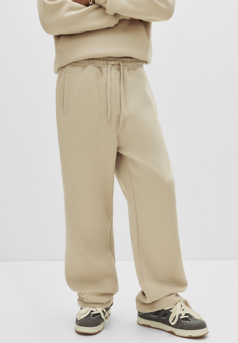 Beige sweats met een relaxte pasvorm, elastische tailleband en trekkoord. Zachte textuur met zijzakken, gecombineerd met donkere schoenen.