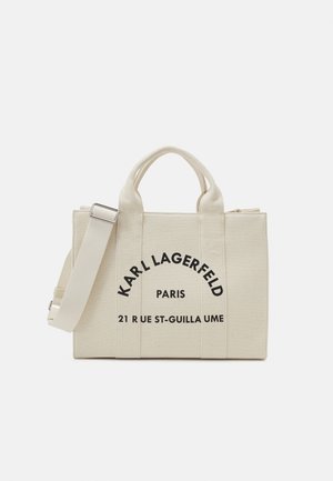 Bolso de lona beige con dos asas superiores, correa ajustable y detalles en texto impreso "KARL LAGERFELD PARIS" en negrita negra.