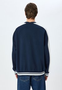 Mörkblå sweatshirt med vita axelaccentuer, ribbad nederkant och ärmslut. Mjukt tyg, lös passform och kontrasterande ränder längst ner.