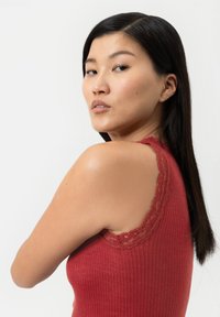 Débardeur rouge à côtes avec des accents en dentelle le long de l'encolure, au design ajusté et à coupe sans manches, présenté sur un modèle avec des cheveux raides et foncés.