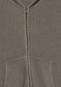 Pletený cardigan na zip v taupe barvě, s vysokým límcem, dvěma předními kapsami a hladkým zipem s kovovým táhlem.