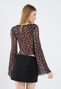 Black floral top with long, flared sleeves, featuring a sheer texture adorned with small red and blue flowers; paired with a black skirt.