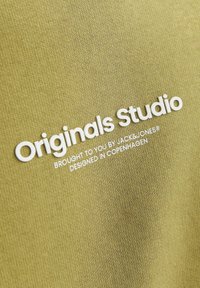 Olivengroen stof met verhoogde witte tekst: "Originals Studio, aangeboden door JACK & JONES, ontworpen in Kopenhagen."