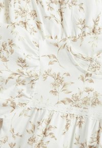 Leichtes Stoffkleid mit einem beigen Blumenmuster auf weißem Grund, verziert mit gerafften Details und Spitzenakzenten.