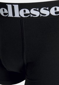 Schwarze Baumwoll-Boxershorts mit einem weichen Bund, der weiße Markenbeschriftung zeigt, glatter Textur und taillierter Passform.