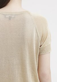 Kortärmad, guldfärgad metallisk stickad topp med en mjuk textur, med raglanärmar och en rund halsringning.