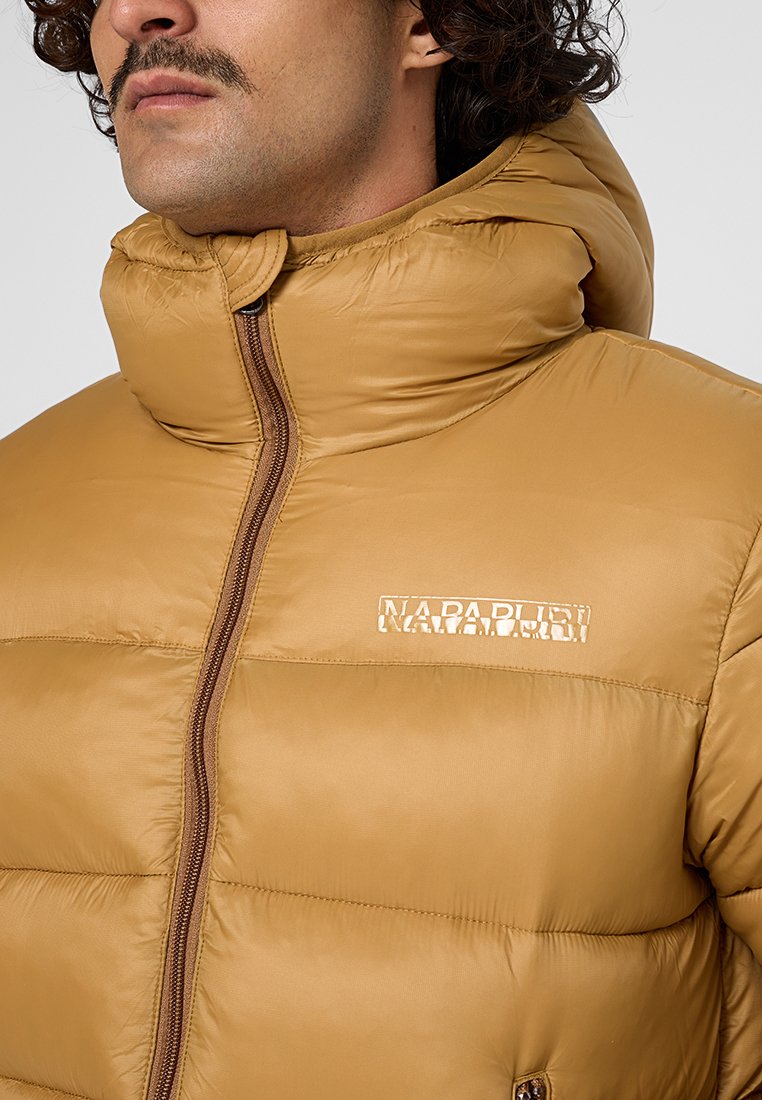 Giacca puffer beige con colletto alto, cuciture orizzontali e chiusura con zip. Il logo è stampato in un colore chiaro sul petto.