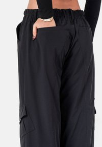 Zwarte cargobroek met een elastische tailleband, zijzak en een soepele, lichte stof. Heeft een ontspannen pasvorm en utility-stijl details.