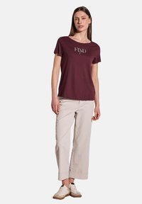 T-shirt bordeaux à manches courtes avec "FIND" imprimé dans une couleur contrastante, associé à un pantalon large de couleur claire et des chaussures décontractées.