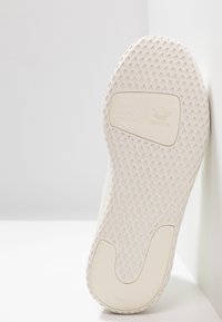 Vita sneakersula med ett texturerat, diamantmönster. Har en logotyp med tre ränder och "Pharrell Williams" präglat på sidan.