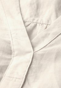 Weißer Leinenstoff mit einem V-Ausschnitt-Design, das subtile Textur und Stickdetails entlang der Ränder und der Knopfleiste aufweist.