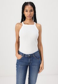 Valge ribaga tank top, millel on laiad rihmad, on ühendatud tumehallide denimite rahakottide ja keskmise kõrge vöökohaga teksadega.