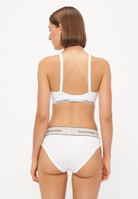 Witte katoen bralette en bikini-slipset met verstelbare bandjes. Opvallende zwarte en beige Calvin Klein logo banden op de tailleband. Gladde textuur.