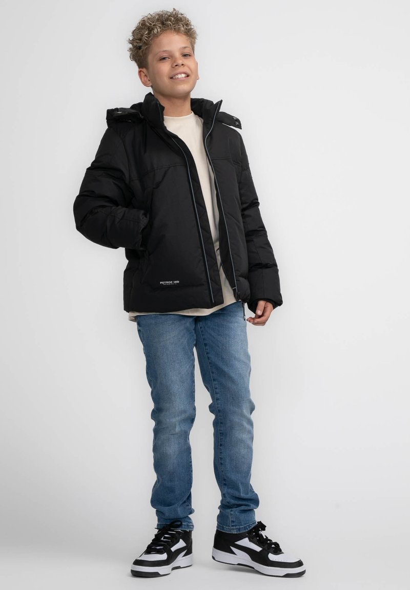Giacca a vento nera con zip frontale, cappuccio e cuciture a contrasto, abbinata a jeans azzurri chiari e sneakers in bianco e nero.
