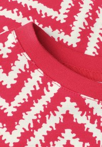 Gros plan d'un tissu tricoté rose et blanc en zigzag avec un col rond et des coutures visibles.