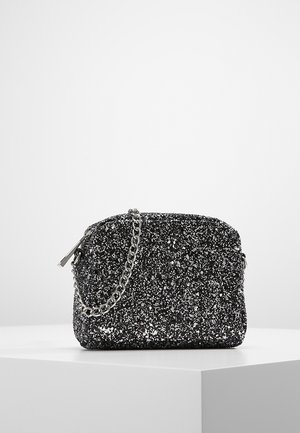 Piccola borsetta nera glitterata con tracolla a catena argentata e cerniera, esposta su un piedistallo bianco su uno sfondo semplice.