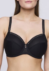 Sostén negro con aros y ribete de encaje festoneado, textura suave, copas estructuradas y cierre frontal con un pequeño acento dorado.