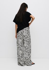 Zwarte oversized t-shirt gecombineerd met wijdvallende broek met een zwart-wit zebra streep patroon. Smooth stof met een ontspannen pasvorm.