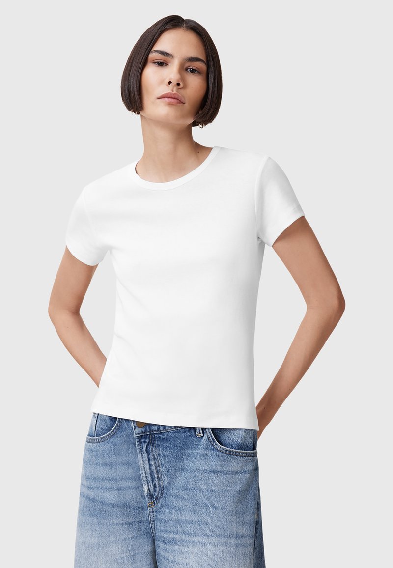 T-shirt bianco in cotone con maniche corte, colletto rotondo, design tailoring e texture liscia, abbinato a pantaloni shorts in denim azzurro chiaro.