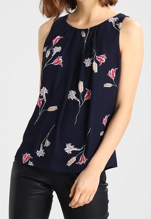 Ærmeløs navy top med lyserøde og beige blomsterprint, båret med sorte læderbukser, frontplisseringsdetalje nær halsudskæringen.