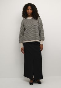 Pull en tricot dans un motif pied-de-poule gris et beige, avec une coupe décontractée et des manches larges, associé à une jupe maxi noire avec une fente sur le côté.