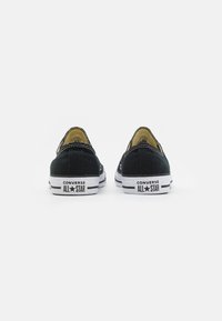 Czarne płócienne trampki z gumowymi podeszwami, wzmocnionymi szwami i białymi akcentami. Posiadają branding "Converse All Star" na pięcie.
