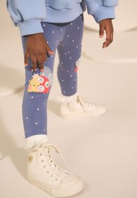 Leggings bleus à pois blancs, ornés d'un patch taco coloré sur le genou. Associés à des baskets montantes blanches et des poignets en dentelle.