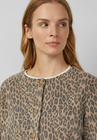 Luipaardprint jasje in beige en bruin, met een ronde halslijn en knoopsluiting. Zachte, gestructureerde stof met contrasterende witte accenten.