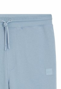 Jasnoniebieskie dresy wykonane z miękkiego materiału, z elastyczną talią na sznurek, boczną kieszenią oraz małą wytłoczoną metką logo.