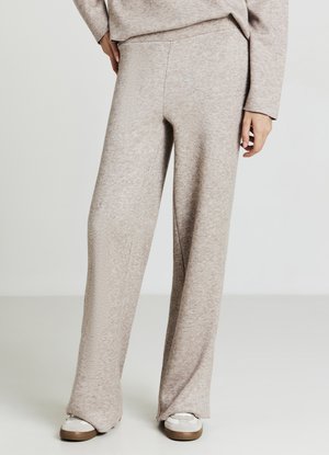 Hellbeige, weit geschnittene Hose aus einem weichen, strukturierten Material. Verfügt über einen taillierten Bund und wird mit weißen Sneakers kombiniert.